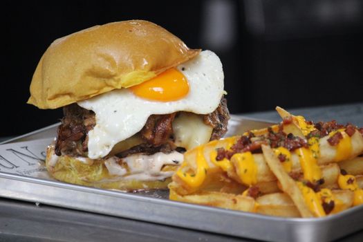 Gourmet burger with fried egg and loaded cheese fries on a metal tray.