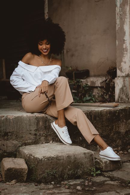 Confident woman in casual attire smiling while sitting on concrete outdoors.