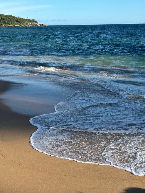 Free Peaceful tropical beach with waves lapping the shore under a clear sky. Stock Photo
