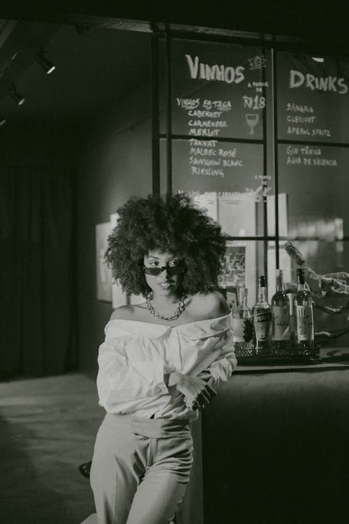Grayscale Photo of Posing Woman in Off-shoulder Dress Leaning on Bar Counter Looking Away