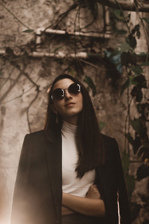 Portrait Photo of Woman in Black Sunglasses and Black Coat Posing With Her Arms Crossed