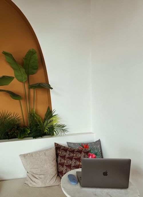 Free A cozy cafe corner with a laptop, cushions, and vibrant plants creating a relaxed workspace. Stock Photo