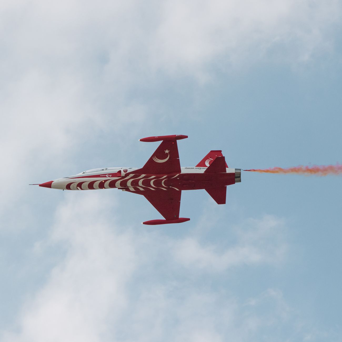 A vibrant Turkish fighter jet performing with colorful smoke trails against a clear blue sky.