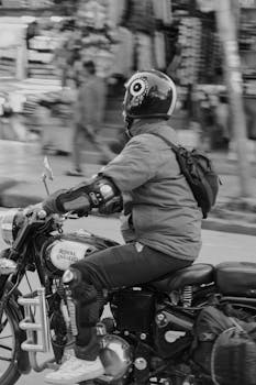 Black and white photo of a motorcyclist on a Royal Enfield bike in urban street.