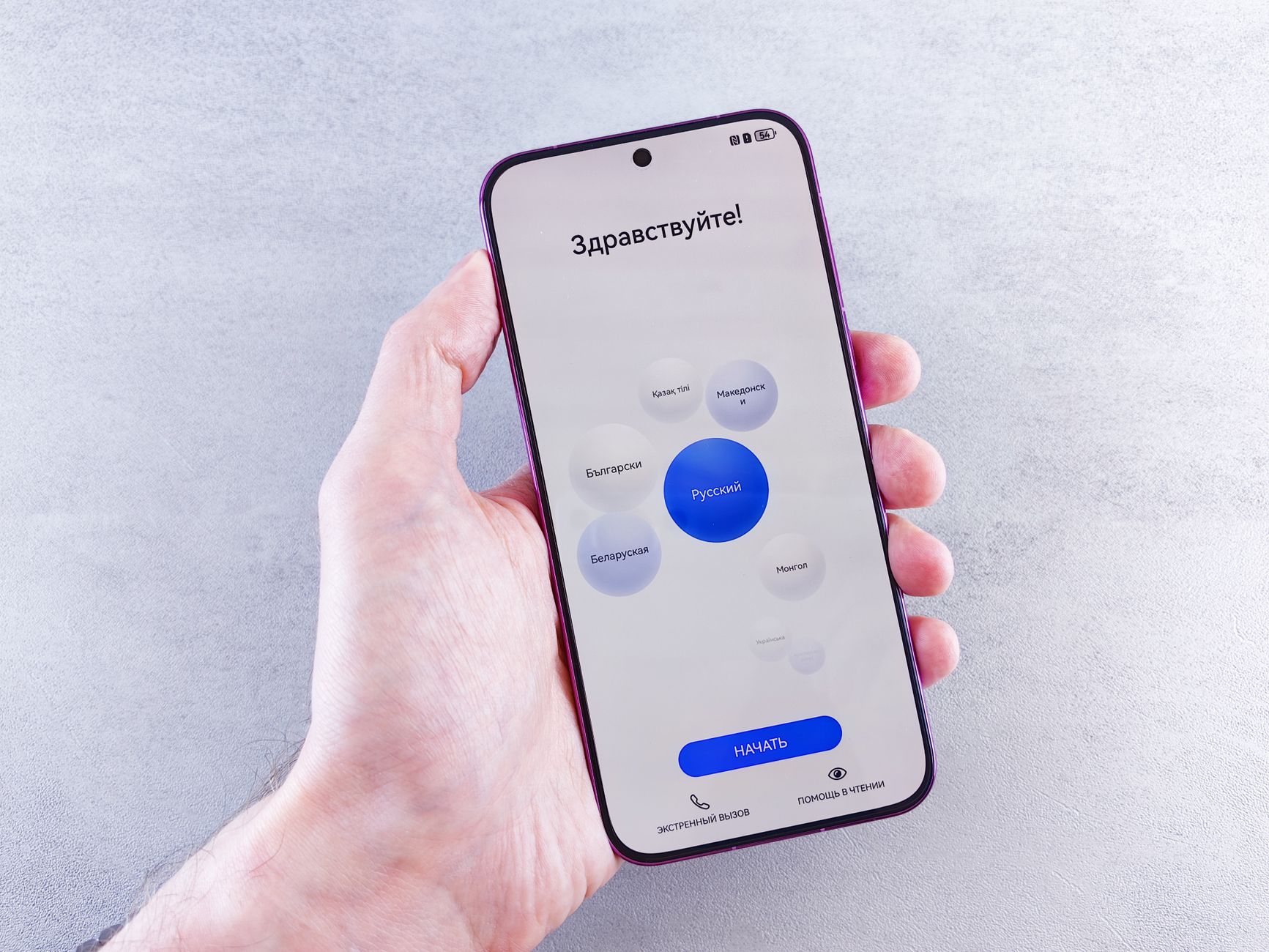 Close-up of a hand holding a smartphone with language selection screen in Cyrillic.