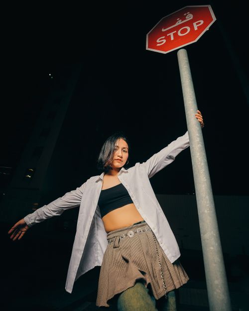 Free Stylish young adult poses confidently at night by a street sign, showcasing modern urban fashion. Stock Photo