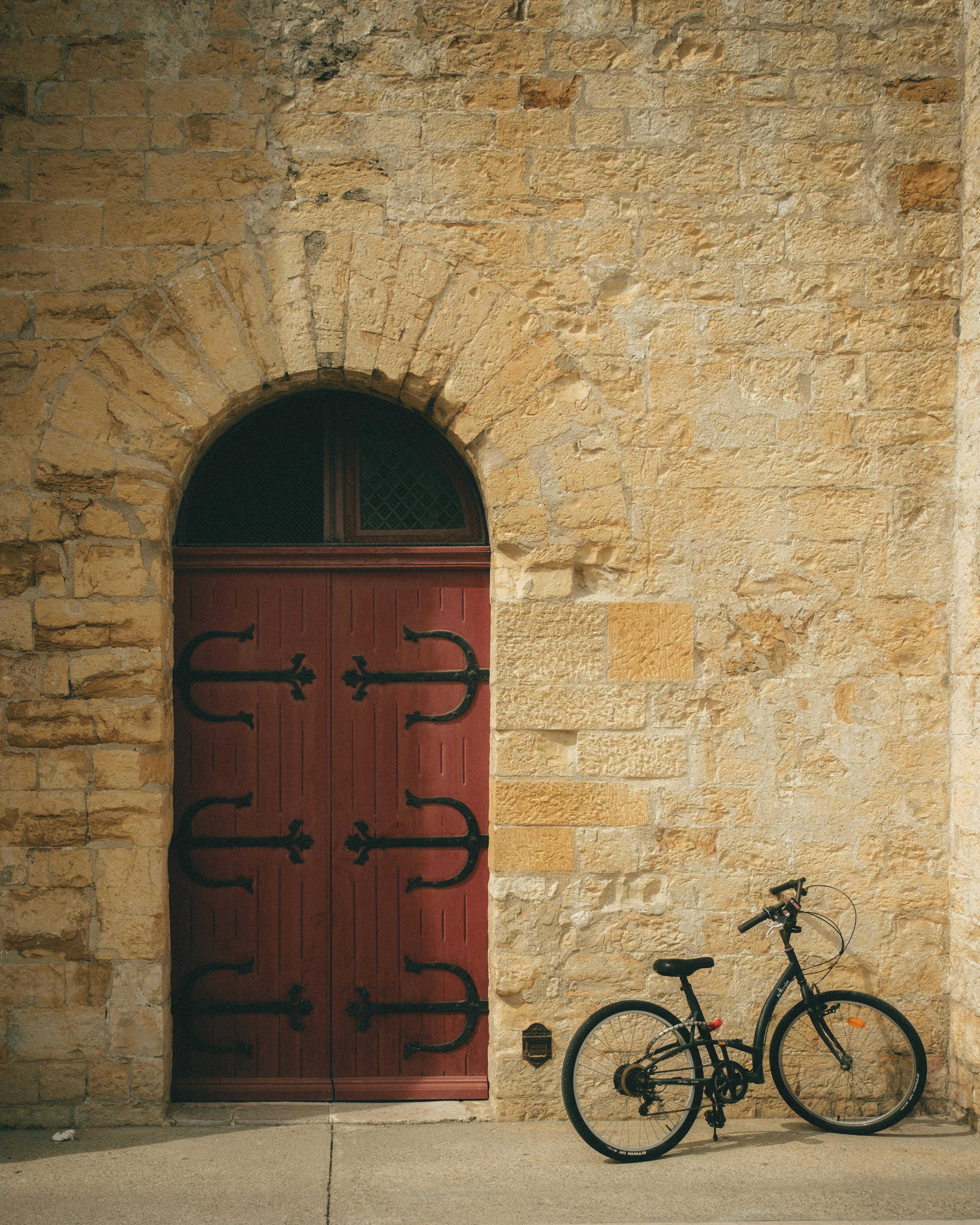 Bicycle rests against vintage door in sunny, rustic stone building scene.
