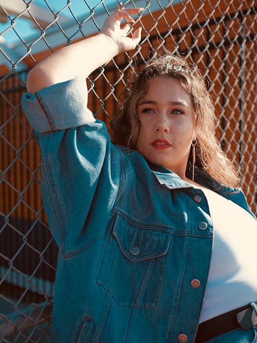 Woman Wearing a Blue Denim Jacket Leaning on Chain Link Fence