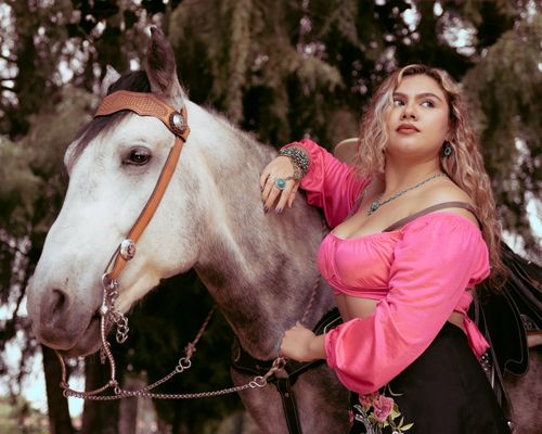 Free A woman with curly hair in a pink top poses confidently with a white horse outdoors. Stock Photo