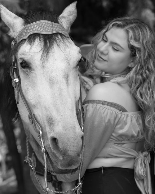 Free A woman with curly hair embraces a white horse in an outdoor setting, showcasing a bond between human and animal. Stock Photo