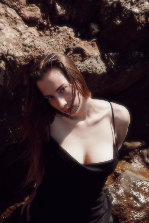 Free Elegant woman in black dress by rocky shoreline, natural beauty. Stock Photo