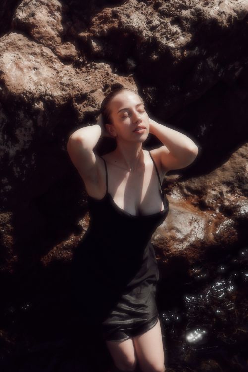 Free Woman enjoying a serene moment by rocky waters, bathed in sunlight. Stock Photo