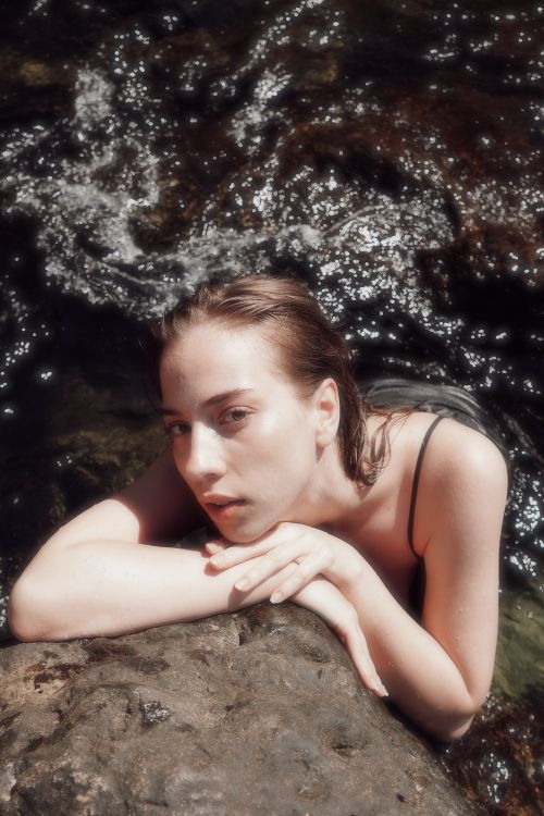 Free Young woman in water, resting on a rock, serene and relaxed atmosphere. Stock Photo