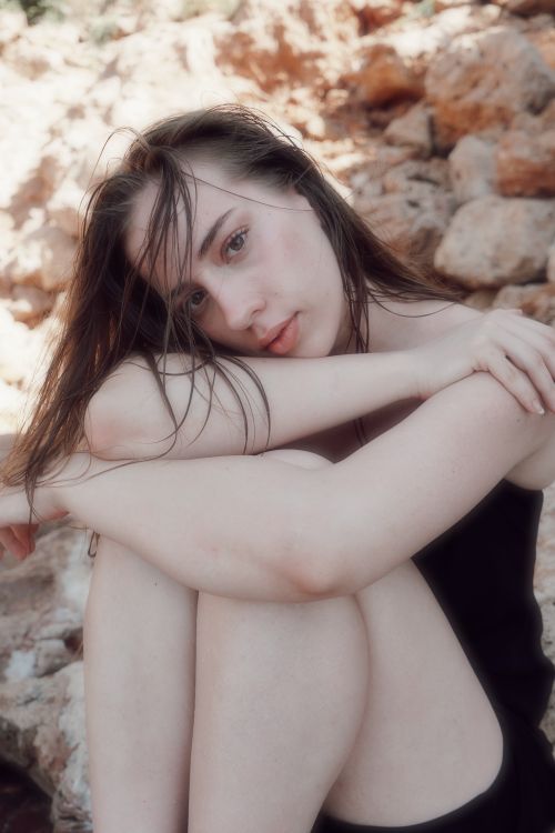 Free A thoughtful woman with wet hair sitting against a rocky background outdoors. Stock Photo