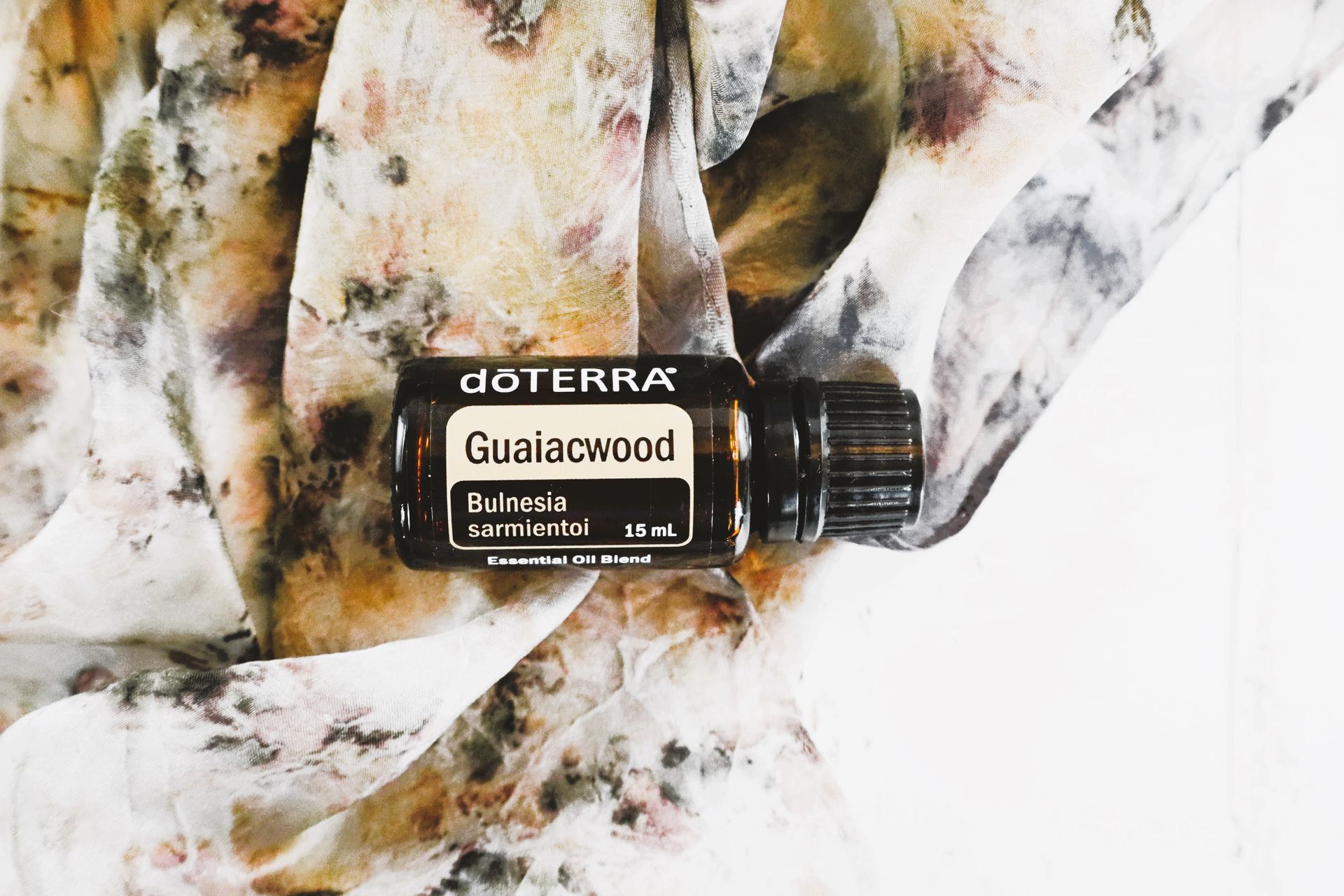 Flat lay of doTERRA Guaiacwood essential oil on earthy fabric background.
