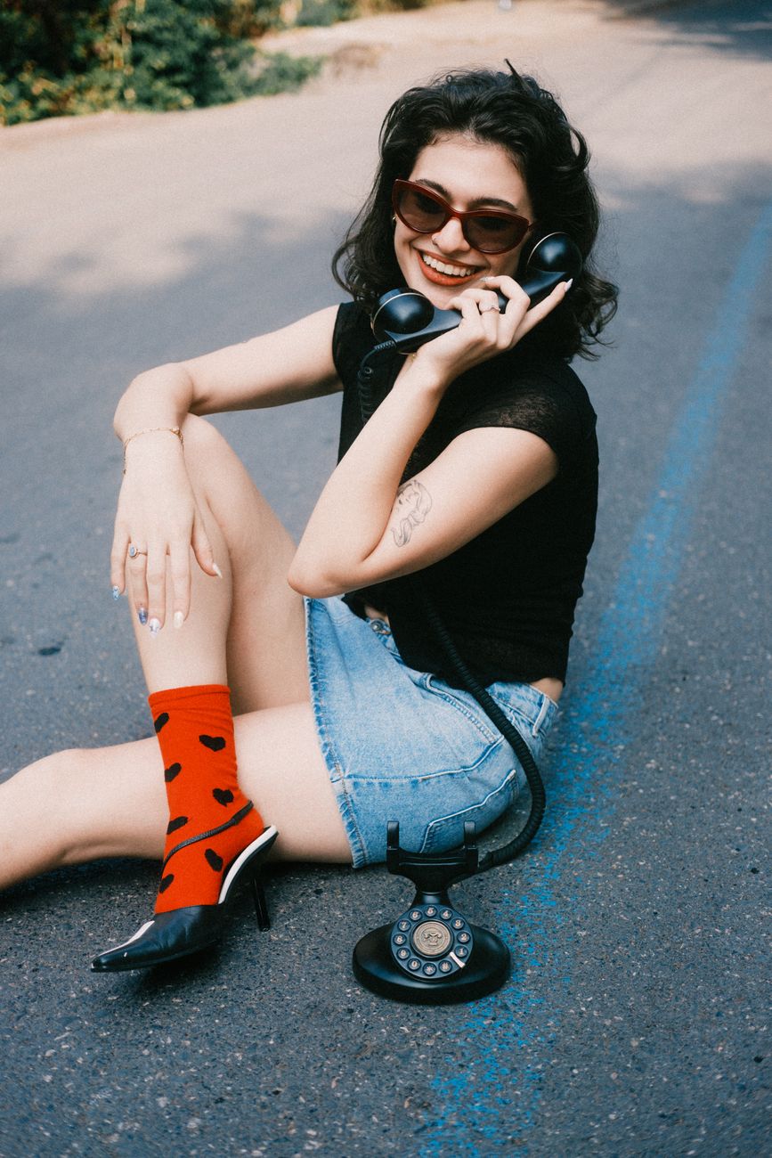 Mulher sorridente posando com um telefone vintage em um dia ensolarado ao ar livre.