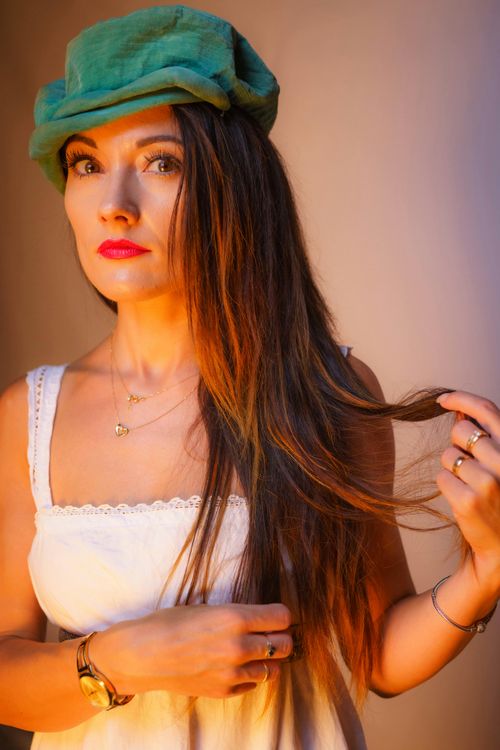 Free Stylish woman in green hat and white dress, showcasing jewelry with elegant pose. Stock Photo