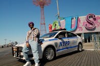 在纽约科尼岛，一名时尚男子戴着墨镜在警车旁摆姿势
