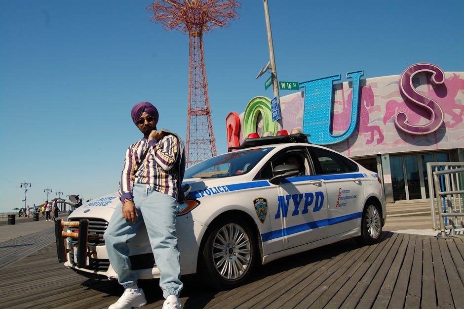 A stylish man in sunglasses poses by a police car at Coney Island, NYC.
