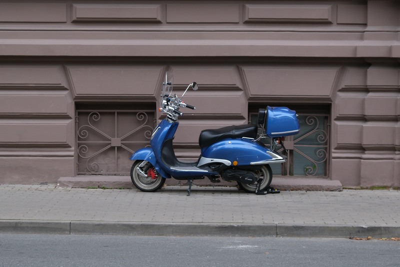 Blue moped parked by an ornate historic building in Riga, Latvia, showcasing urban architecture.