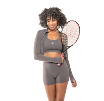 Afro-haired female athlete in gray sportwear holding tennis racket on white background.