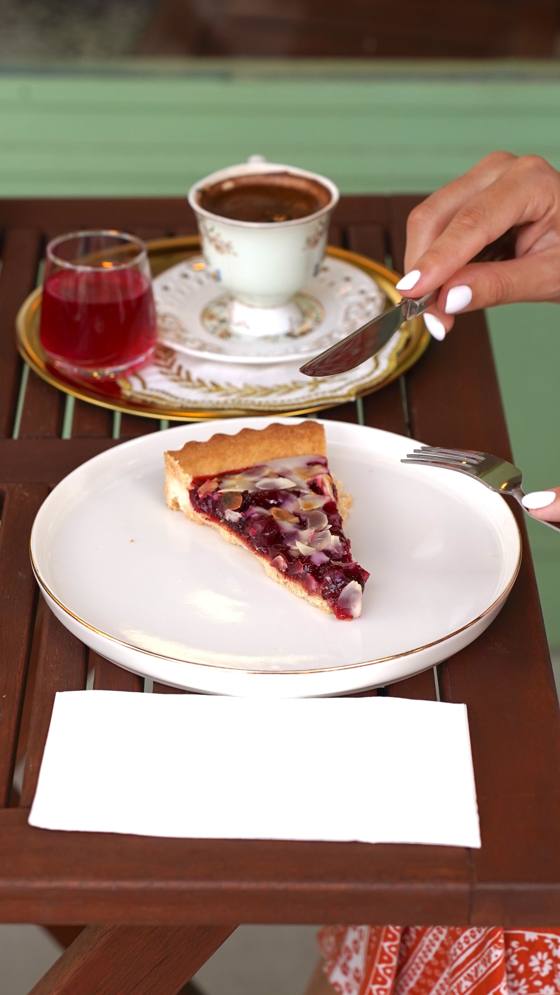 Slice of cherry pie with coffee and juice setup on an outdoor cafe table.