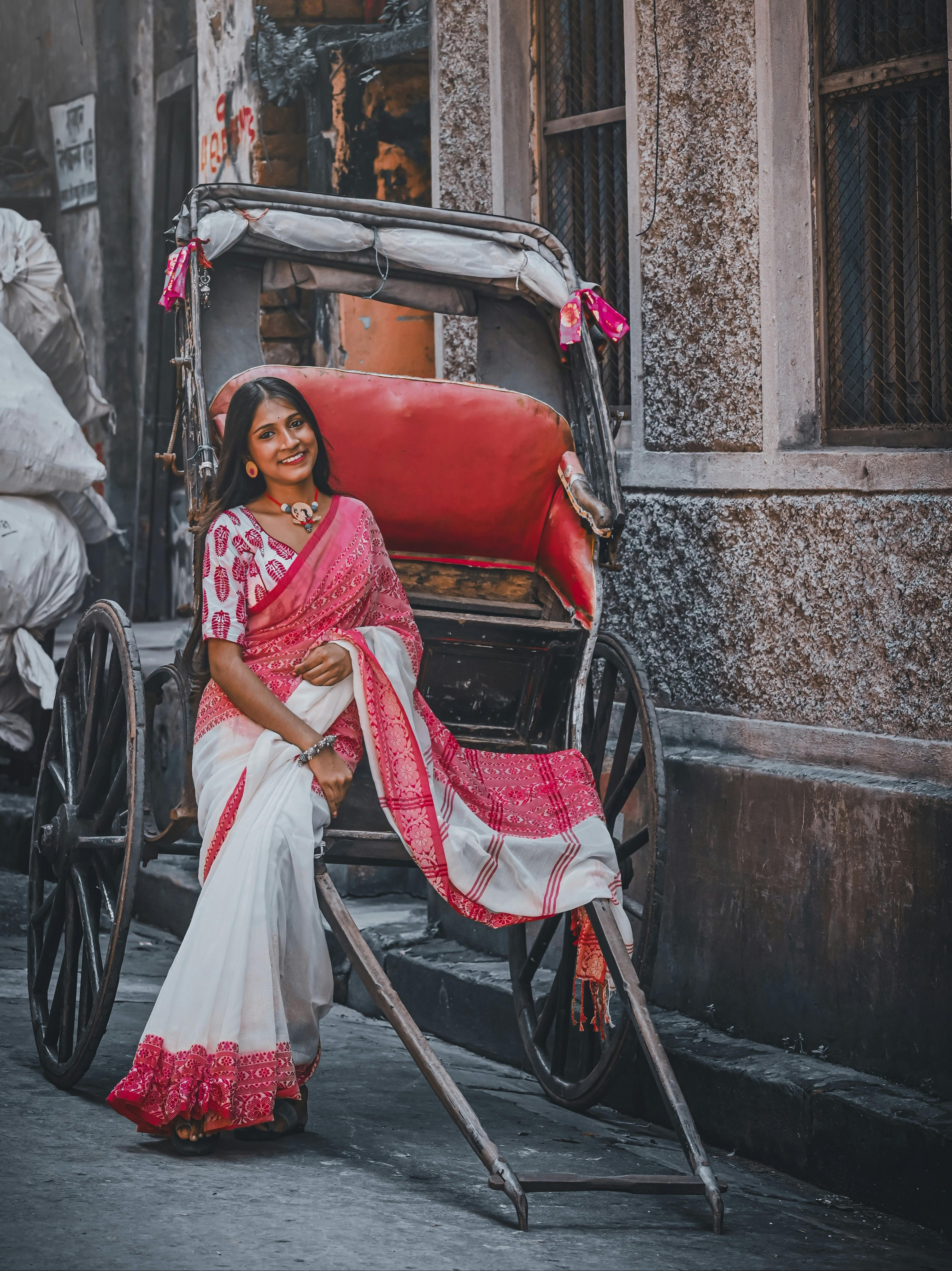 Elegant woman in a bridal saree posing with a rickshaw on a Kolkata street, exuding cultural charm.