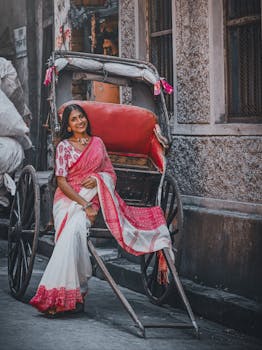 Elegant woman in a bridal saree posing with a rickshaw on a Kolkata street, exuding cultural charm.