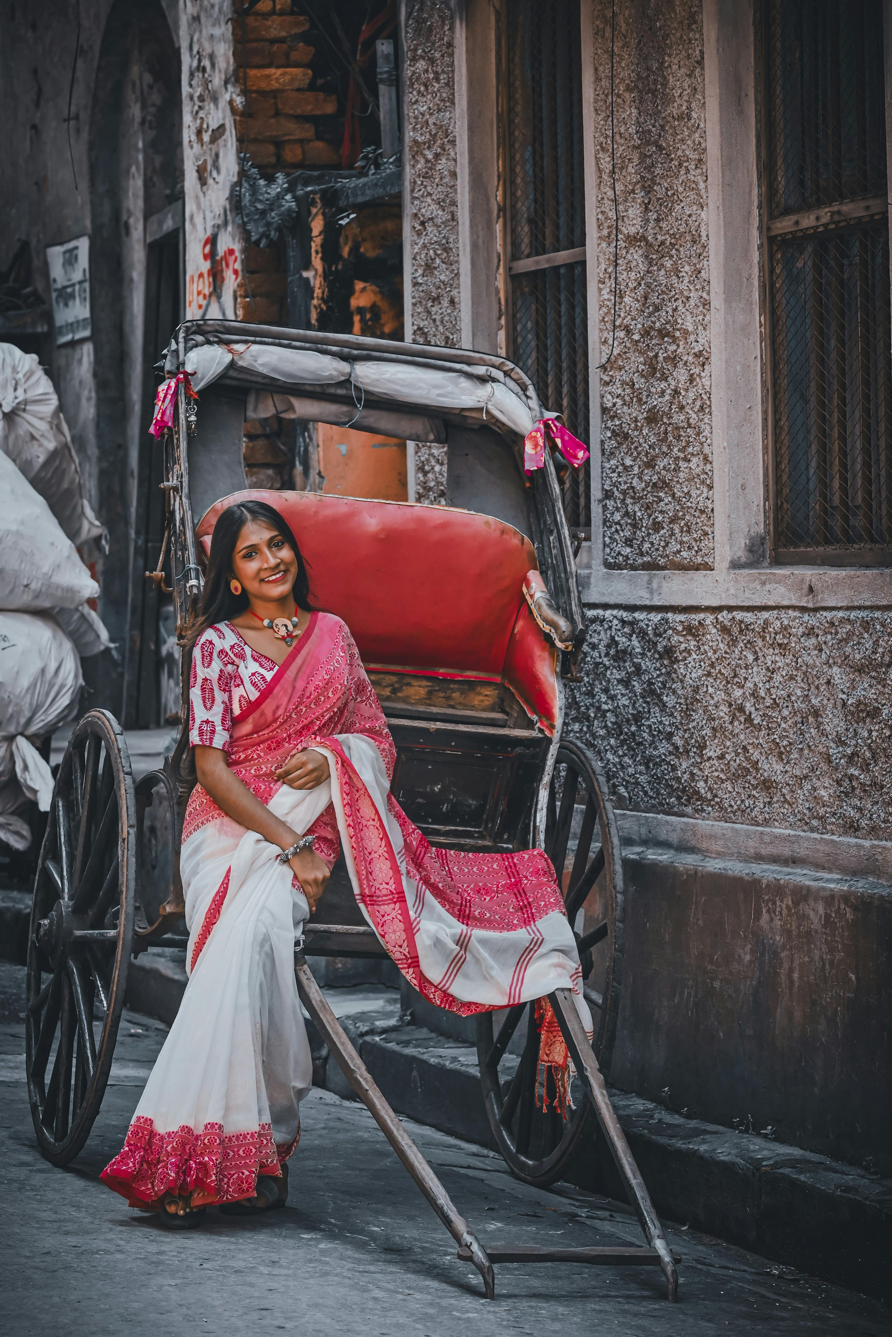 Graceful woman in a vibrant saree poses with a traditional rickshaw in Kolkata's charming streets.