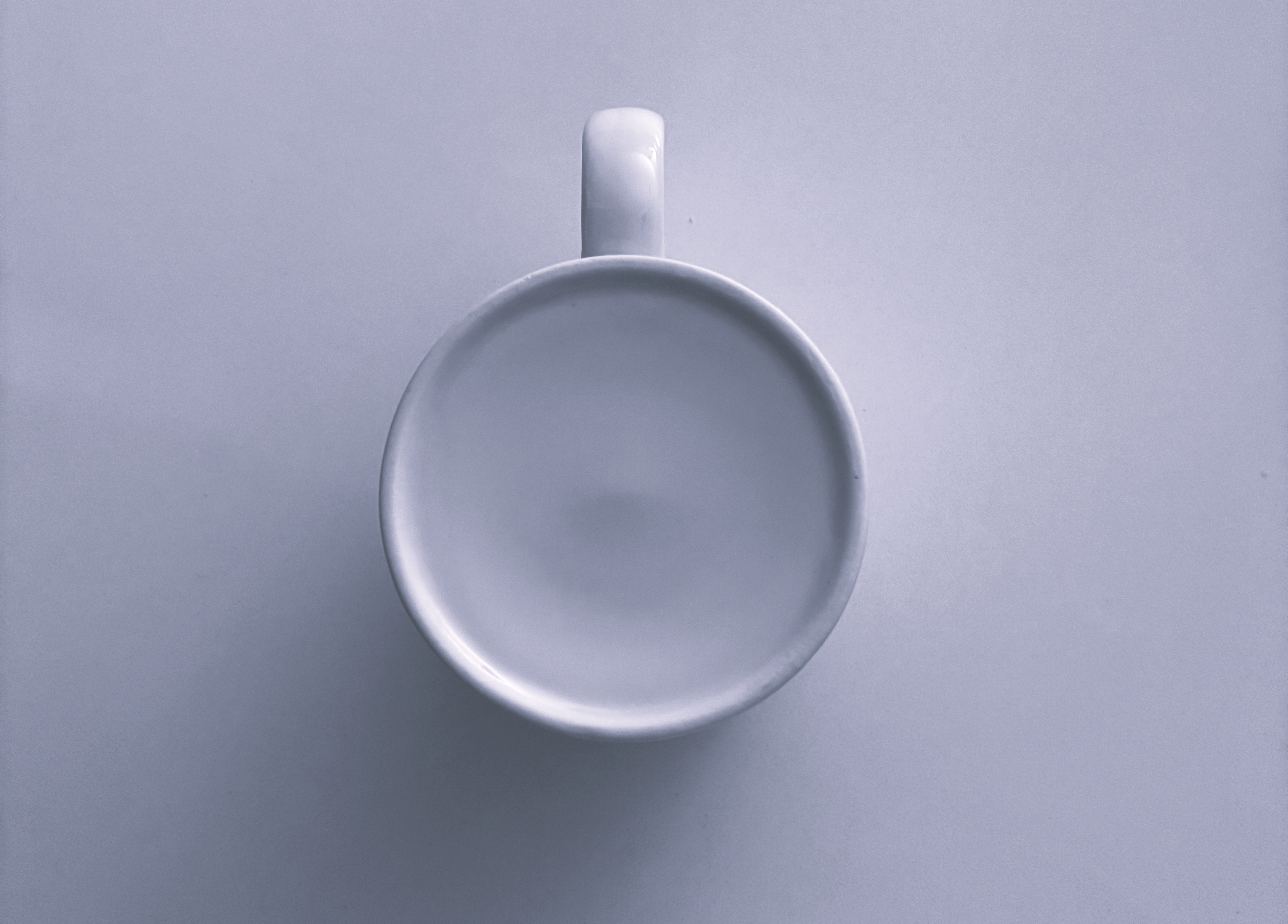 A simple, elegant top-down view of an empty white coffee mug on a white surface.