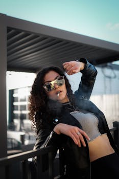 Young woman wearing sunglasses, leaning casually and enjoying outdoor urban setting.
