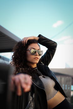 Fashionable woman in sunglasses poses confidently outdoors in an urban setting.