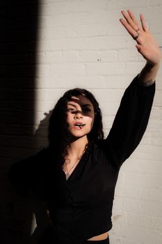 A woman in black poses against a brick wall, casting dramatic shadows.
