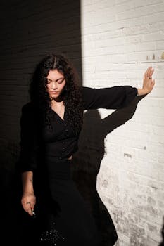 Artistic portrait of a woman with curly hair against a white brick wall in dramatic lighting.