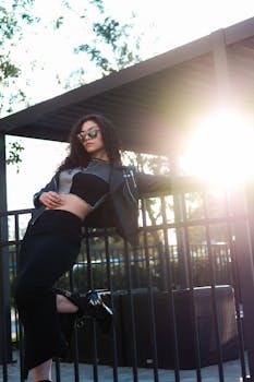 Stylish woman in sunglasses poses confidently outdoors at sunset, exuding modern urban vibes.
