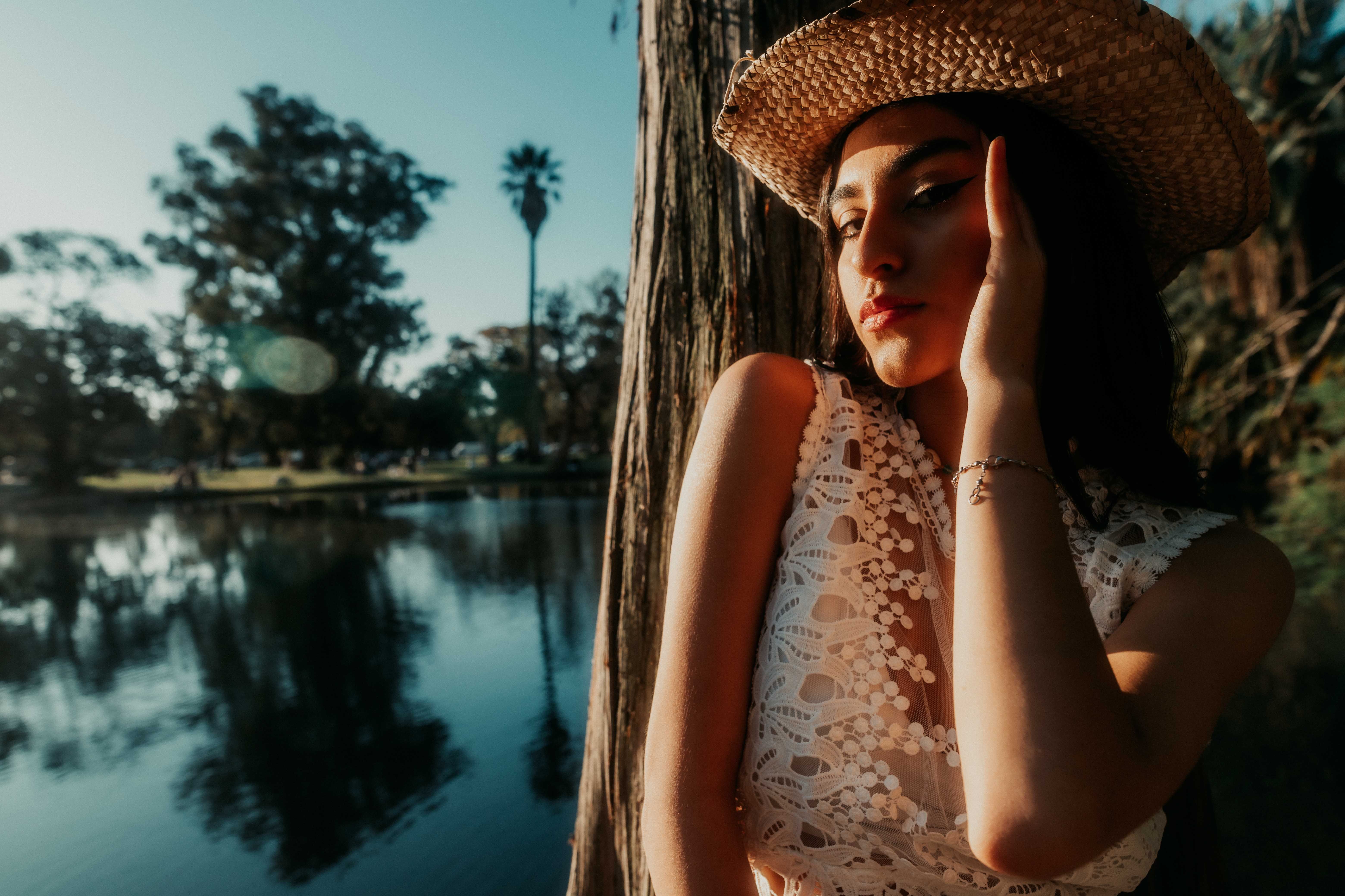Young woman in a straw hat enjoying the sun by the serene lake reflecting trees.