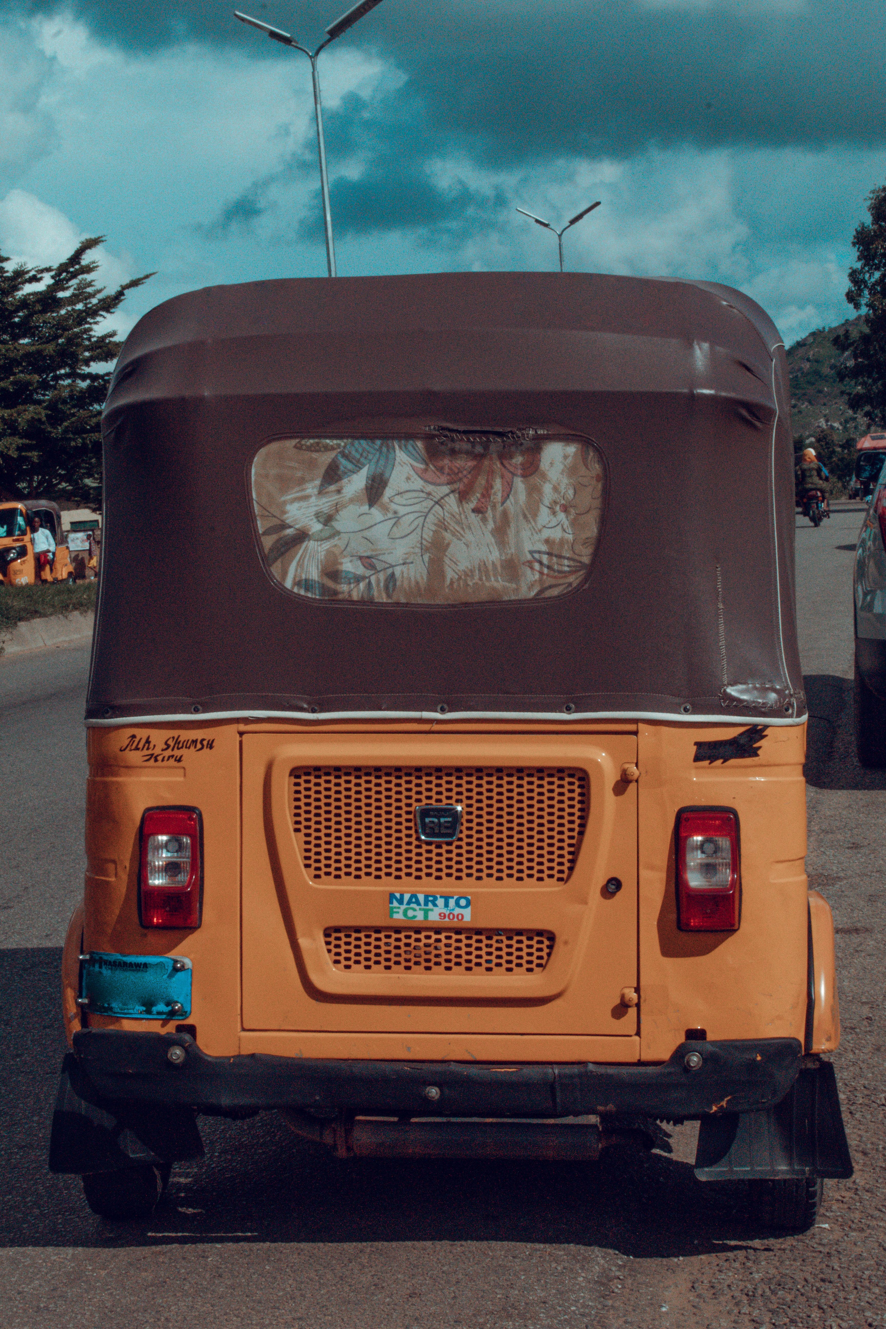 A yellow rickshaw on a street in Abuja, Nigeria, under a cloudy sky.