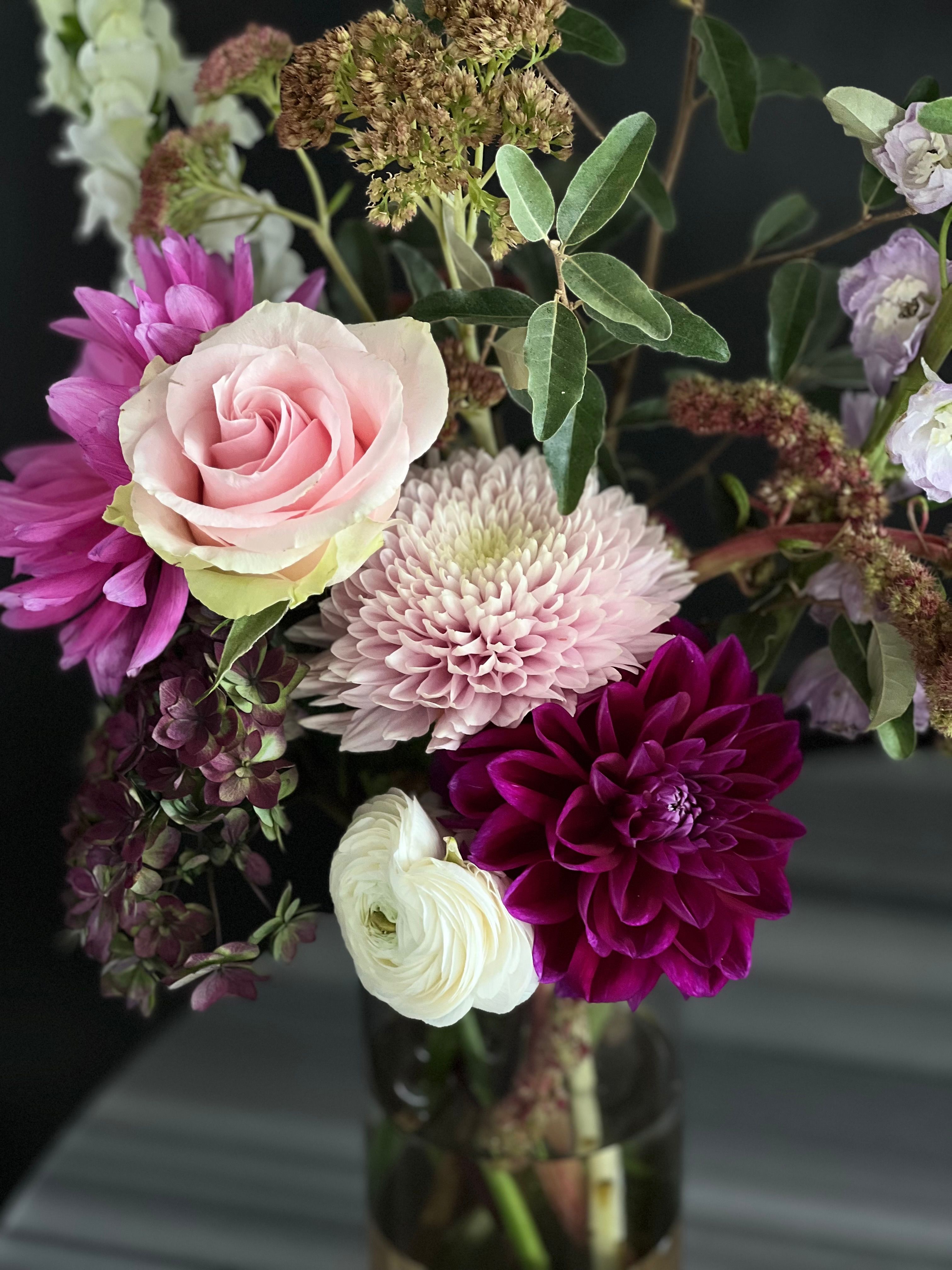 A loose seasonal bouquet of cosmos, dahlias, and grasses on a worn wood table.