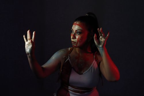 Free A woman with creative face paint reaches dramatically into the shadows under vibrant lighting. Stock Photo