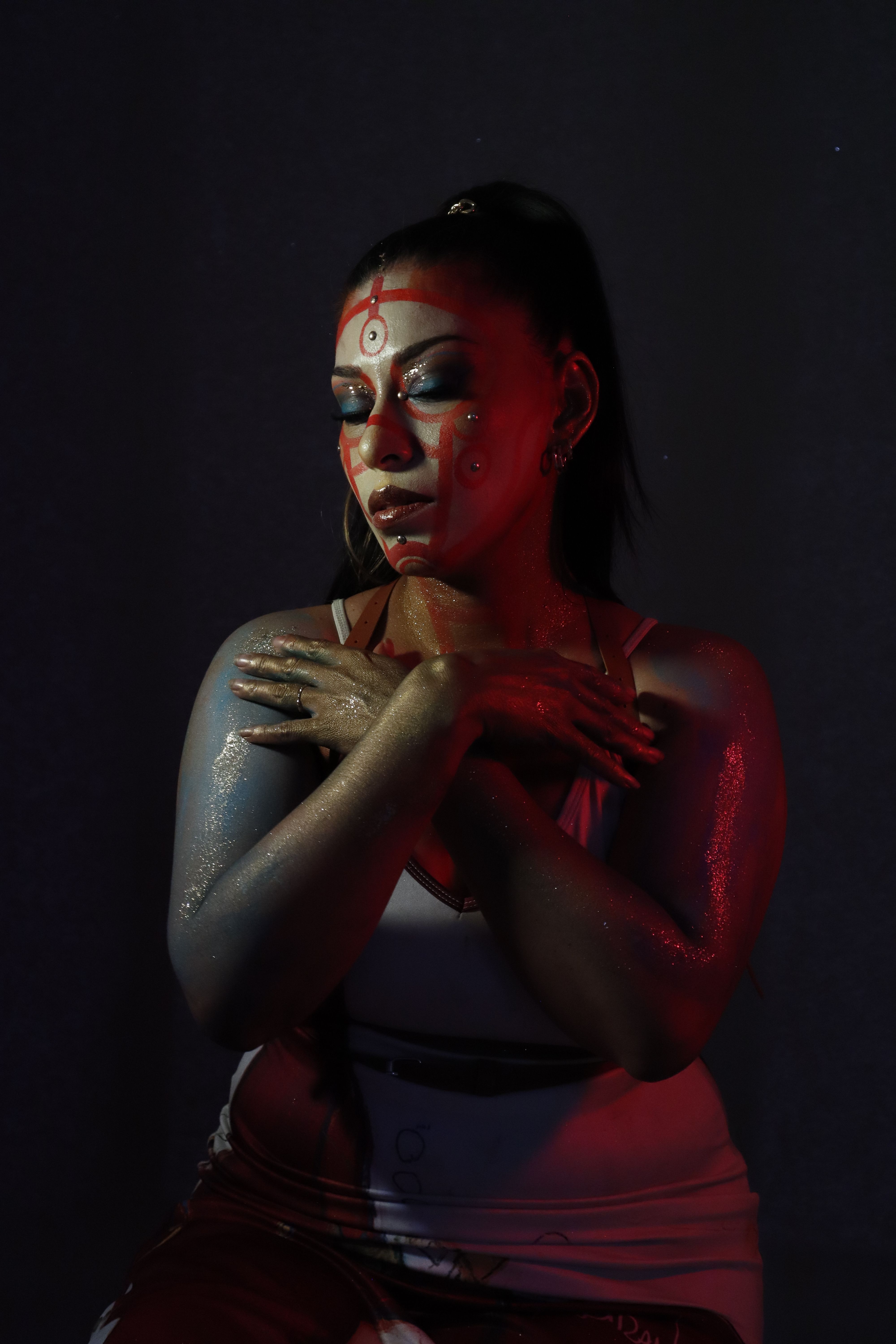 Captivating portrait of a woman with artistic makeup, crossed arms, in dramatic red lighting.