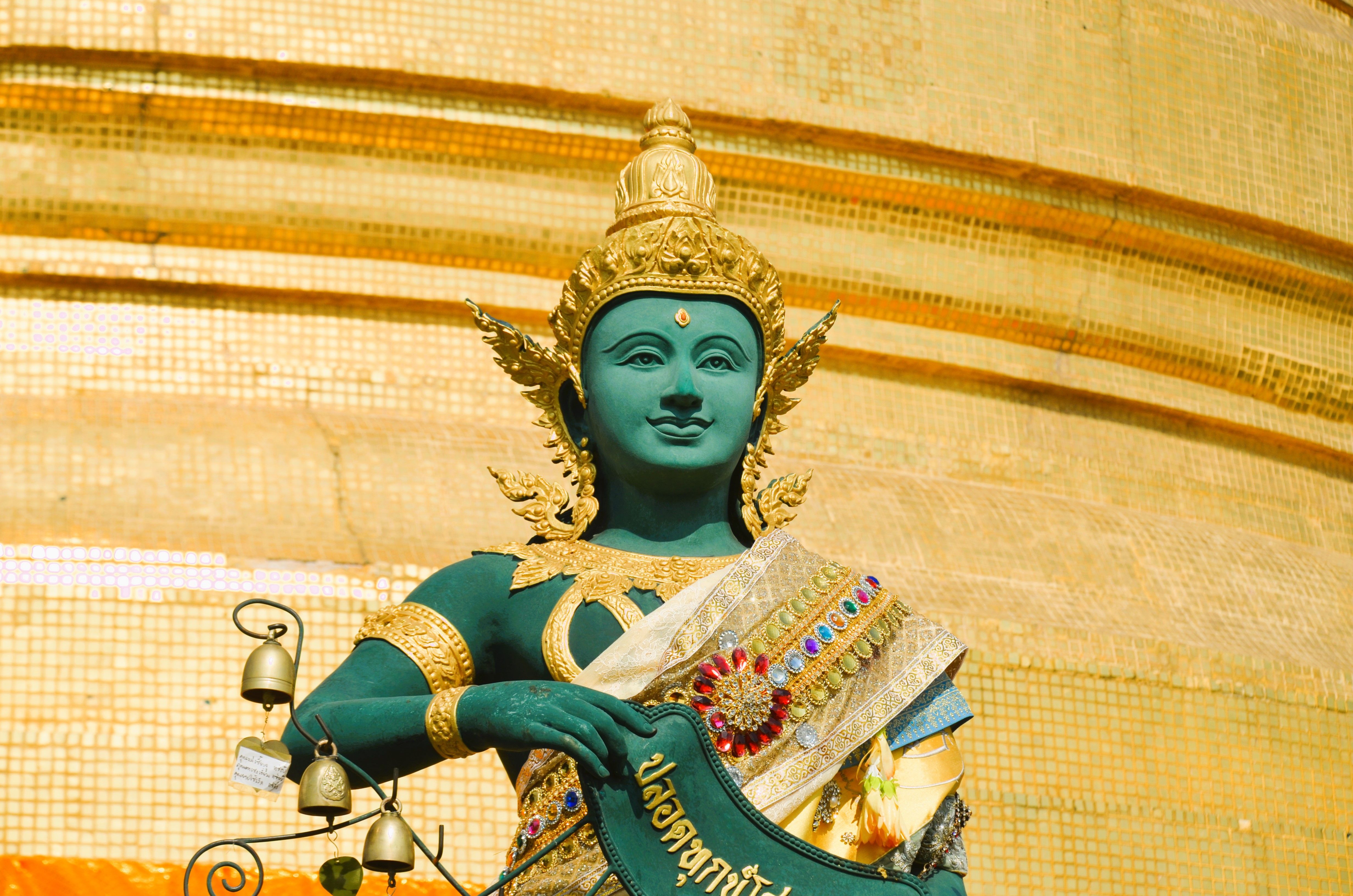 Statue of a deity adorned in jewels at a golden temple, bathed in sunlight.
