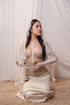 Elegant bride in satin dress with lace details holding a candelabra, creating a romantic and sophisticated atmosphere.