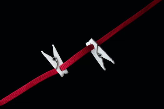 Minimalist photo of white clothespins clipped on a vibrant red cord against a black background.