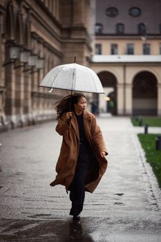 Stylish woman with umbrella walking on a rainy day in the city street.