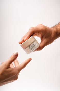 Close-up of hands exchanging a jar of luxury skincare cream on a white background.