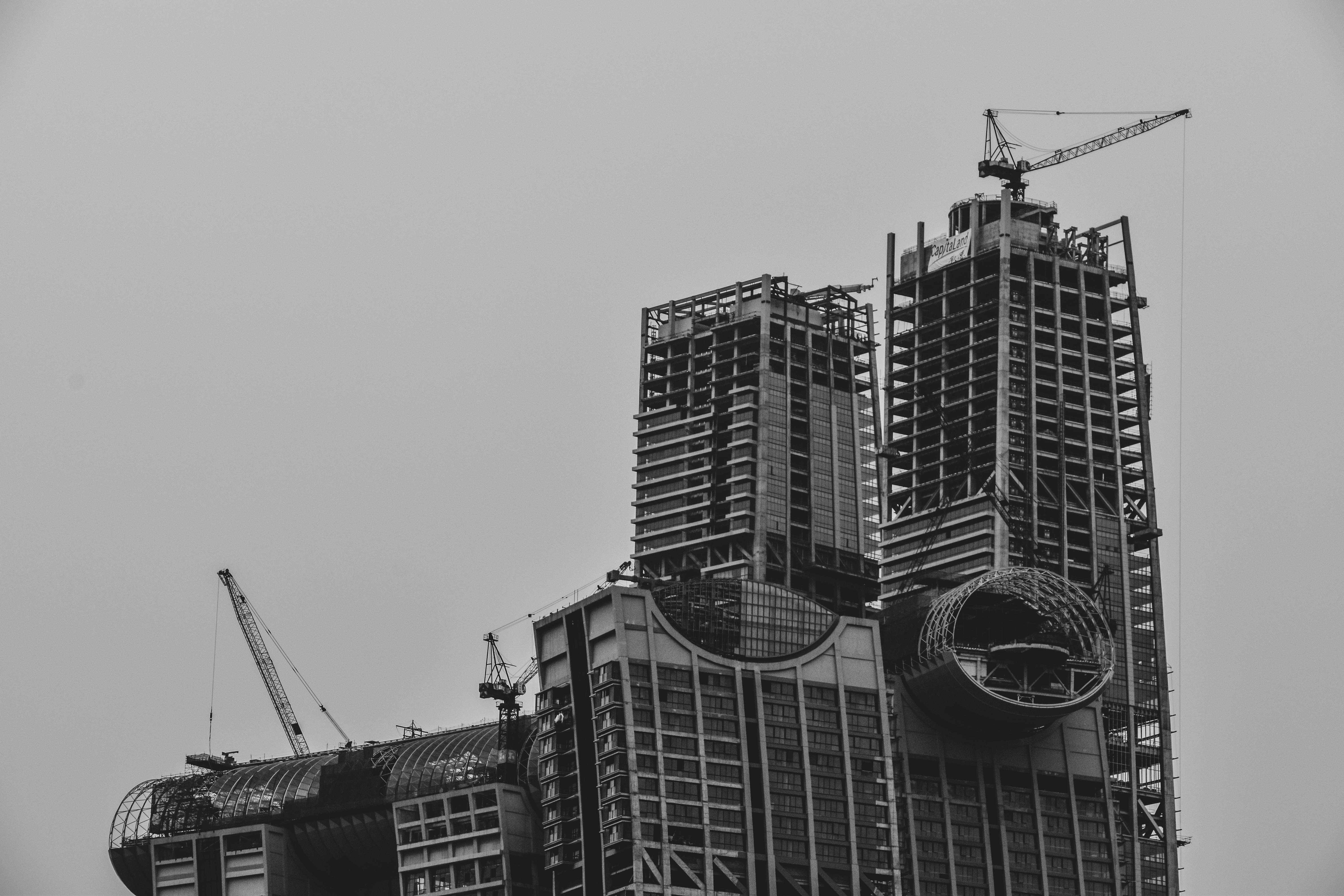 grayscale photography of high rise building with tower cranes