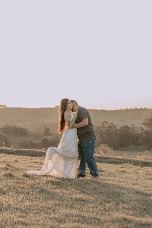 Free A couple sharing a romantic kiss during sunrise in a beautiful countryside setting. Stock Photo