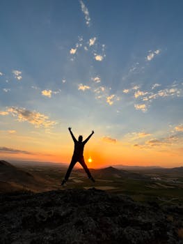 A person silhouetted against a vibrant sunset on a mountain peak, symbolizing freedom and adventure.