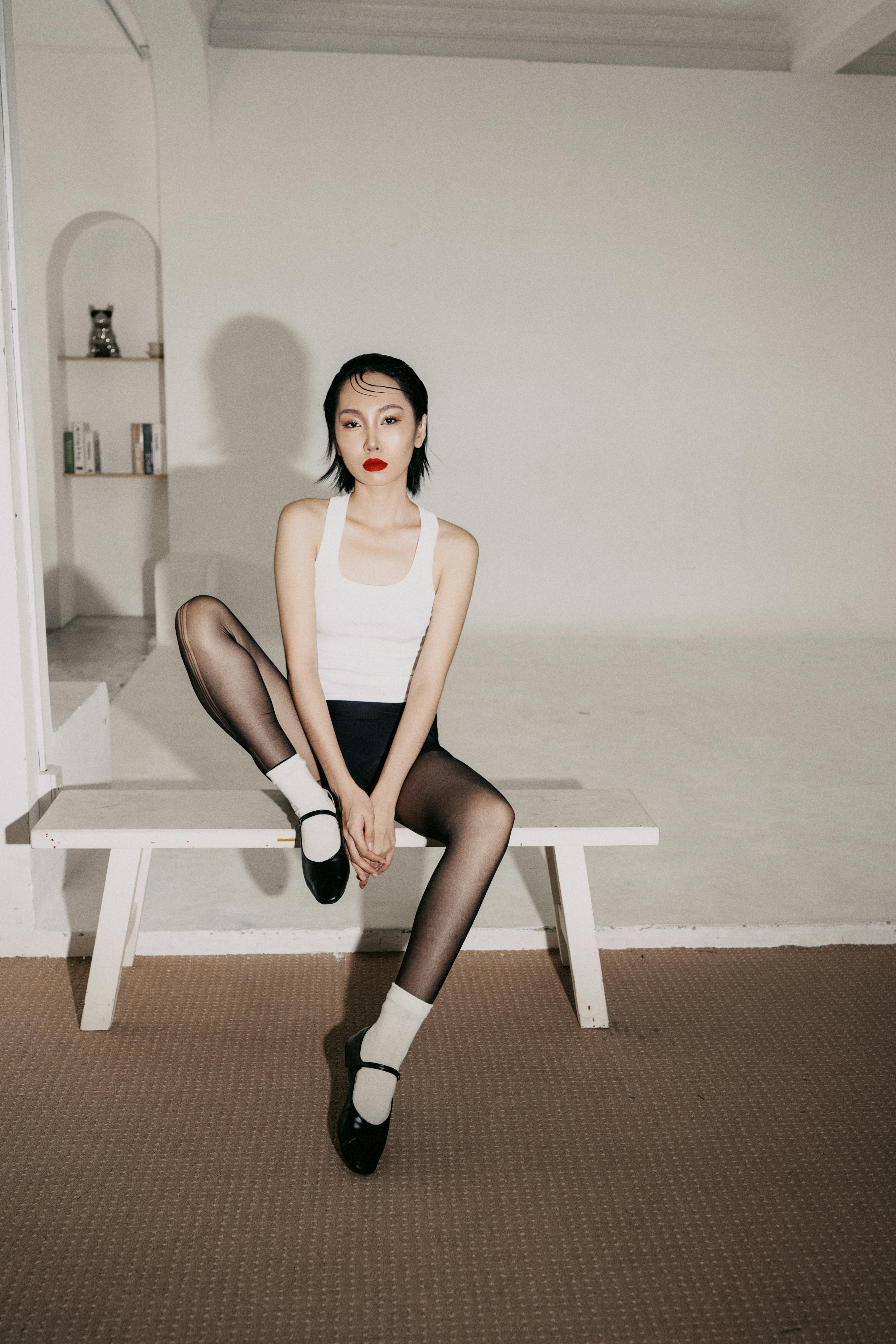 Artistic portrait of a woman in monochrome attire seated indoors in a minimalist style.
