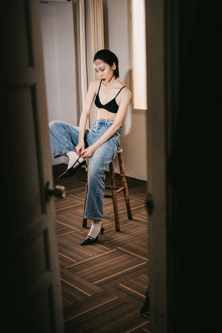 Fashion photo of a woman in denim jeans and black top, captured indoors with a relaxed pose.